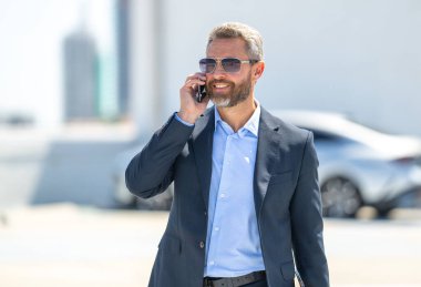 Başarılı bir iş adamı açık havada telefonla konuşuyor. İş adamı dışarıda telefon kullanıyor. Takım elbiseli olgun iş adamı. Şirket işi. Takım elbiseli zengin iş adamı. Açık hava iş portresi