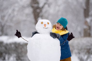 Çocuk kışın kardan adam için kartopu yapıyor. Çocuk karda oynuyor. Açık havada aktif kış oyunları. Çocuk karla oynarken eğleniyor. Çocuklar için açık havada kış tatili. Güneşli kış gününde çocuk oyunu