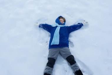 Kar meleği yapan bir çocuk. Karlı melek kanatlarıyla karda yatan mutlu çocuk. Karda kaygısız bir çocuk. Noel tebrik kartı ile evlen. Kışlık giysili tatlı çocuk karda yatıyor. Kış Tatili