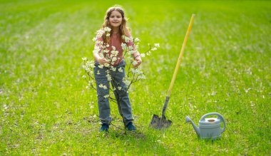 Çocuk dikme ağacı. Çocuk kürek ve su bidonuyla çalışıyor. Çocuk meyve ağacı dikmiş. Bahçıvan çocuklar. Çocuk ağaç dikmek ve onunla ilgilenmek. Elinde kürek olan, ekmeye hazır bir çocuk. Ağaçlarla ilgilenen genç çiftçi