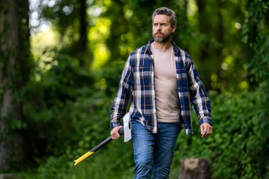 Ekose gömlekli oduncu ve kot pantolonlu. Yaz tahtasında büyük bir balta taşıyor. El işi. Doğal ortam. Ormanda baltası olan oduncu. Çalışkan adam. Baltası ya da baltası olan kaba sakallı bir adam.