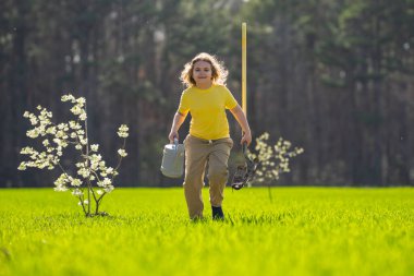 Bahçede çalışan bir çocuk. Bahçede yetişen ağaç ve bakım bitkisi. Bahçıvanlık sezonu. Bitki yetiştiren bir çocuk. Bahçe işleri. Çocuk bahçede meyve ağacı suluyor. Çocuk ağaç dikiyor. Bahçede bahar