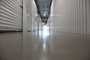Modern bir depolama tesisinin içinde uzun bir koridor. Kapıları metal kapaklı boş depo koridoru. Kiralık temiz ve güvenli depolama birimleri. Sanayi ile simetrik depolama koridoru