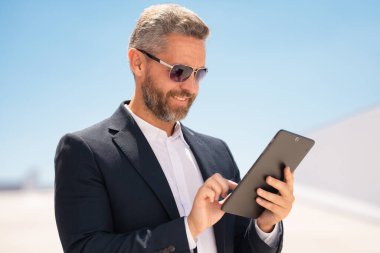 Açık havada tablet kullanan mutlu bir iş adamı. Tabletle başarılı bir iş adamı. Dışarıda tablet üzerinde çalışan bir iş adamı. Zarif iş adamı tableti kontrol ediyor. Dijital aygıt kullanan işadamı