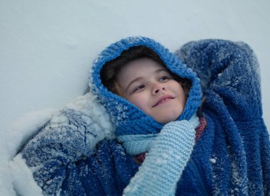 Kışlık giysili çocuk kış tatilinde kar yığınında yatıyor ve gülüyor. Kış çocukları mutluluğu. Kışlık giysili tatlı çocuk karda yatıyor. Kış tatili. Kış tatili macerasında komik çocuk