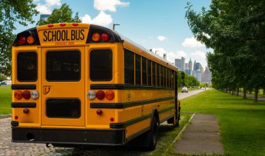 Şehir yolunda park etmiş sarı okul otobüsü. Okul taşıma aracı. Bir yaz şehrinde klasik sarı okul otobüsü. Okul otobüsü şehir parkında sakin bir yolda bekliyor.