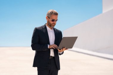 İş adamı dışarıda dizüstü bilgisayar kullanıyor. Dizüstü bilgisayarda çalışan başarılı bir adam. Dizüstü bilgisayarı olan kendinden emin bir iş adamı. İnternette iş. İş adamı laptoptaki verileri kontrol ediyor. Takım elbiseli iş adamı internette çalışıyor.