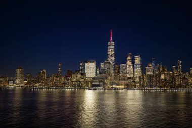Manhattan gece silueti. New York City geniş panoramik silueti. Rıhtım boyunca New York şehri manzarası. Manhattan şehir merkezinin yukarısındaki New York hava şeridi. Gökdelenli New York manzarası