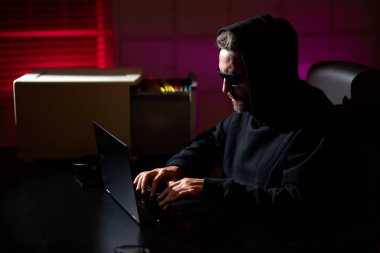 Bilgisayar korsanları siber saldırı sırasında bir gece ofisindeki dizüstü bilgisayarda yazarlar. Hacker şifreli para çaldı. Dijital para korsanı. Siber saldırı. Ofiste laptop kullanan kapüşonlu bir bilgisayar korsanı.