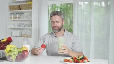 Adam mutfakta dengeli yemek yiyor. Mutfaktaki adamın sağlıklı yeme alışkanlığı. Adam evde temiz ve sağlıklı yemekler pişiriyor. Mutfakta bir erkekle sağlıklı bir kahvaltı anı.