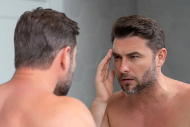 Tıraş olduktan sonra mükemmel cilt teması olan seksi, şehvetli bir erkek. Cilt bakımı kozmetik işlemleri konsepti. Aynaya bakan adam, hassas cilt, kozmetik tedavisi. Cilt bakımı