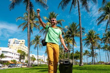 Miami sahilinde bavulla yürüyen bir turist. Yaz tatilinde valizli bir turist. Tropikal şehirde bir turist. Tropik tatil beldesinde bavullu bir turist. Turizm ve seyahat kavramı