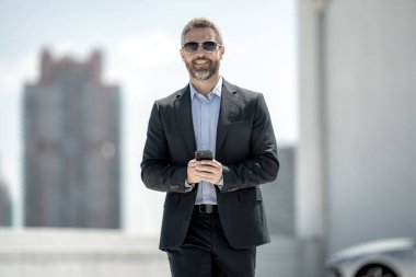 Başarılı bir iş adamı telefonu açık havada tutar. İş adamı dışarıda telefonda konuşuyor. Takım elbiseli olgun iş adamı. Şirket işi. Takım elbiseli zengin iş adamı. Açık hava iş portresi