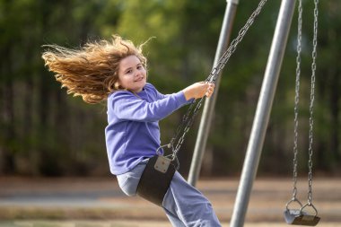 Çocuk parkta salıncakta sallanıyor. Sarı saçlı küçük bir çocuk salıncakta sallanıyor. Salıncakta gülümseyen mutlu çocuk. Mutlu çocukluk anları. Çocuk dışarıda oynuyor. Çocuk salıncakta eğleniyor. Çocuklar için açık hava oyunu