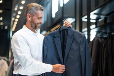 Takım elbiseli, takım elbiseli bir iş adamı. Bir iş adamı mağazada şık bir takım elbise seçer. Modayı takip eden bir müşteri resmi kıyafet alırken ceketi inceler. Klasik kıyafetli çekici bir manken.