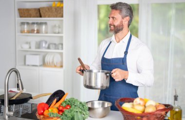 Taze sebze pişiren bir şef. Ev yapımı yemek pişiren bir adam. Mutfakta sağlıklı bir kahvaltı için sebze pişiren bir aşçı. Üniformalı bir adam beyaz bir evde sebze pişiriyor.