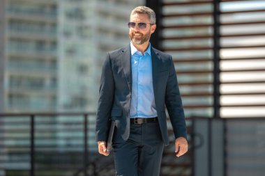 Successful businessman walk with on laptop outdoors. Confident business man hold laptop outside. Mature businessman in suit. Corporate business. Rich business man in suit. Outdoor business portrait