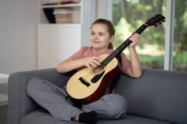 Gitar çalan çocuk. Oturma odasında gitar çalma pratiği yapan bir genç. Çocuk içeride gitar öğreniyor. Müzik dersi sırasında gitarlı bir çocuk. Akustik gitar çalan bir çocuk. Çocuk şarkıları çalışıyor