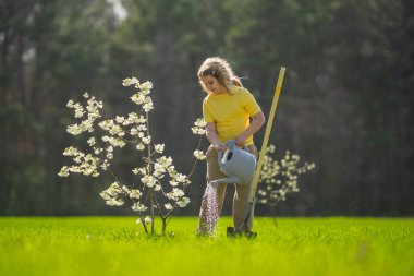 Bahçede çalışan bir çocuk. Bahçede yetişen ağaç ve bakım bitkisi. Bahçıvanlık sezonu. Bitki yetiştiren bir çocuk. Bahçe işleri. Çocuk bahçede meyve ağacı suluyor. Çocuk ağaç dikiyor. Bahçede bahar