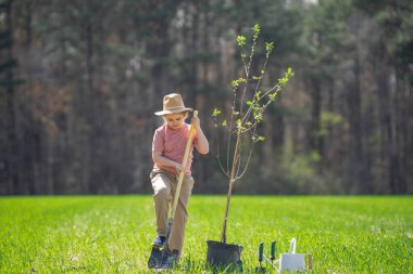 Kürekle ağaç yetiştiren mutlu çocuk. Arka bahçede ağaç yetiştiren bir çocuk. Bahar tarlasında ağaç yetiştiren çocuk. Su kovası ve küreği olan bahçıvan. Bahçe çiftliğinde ağaç yetiştiren çocuk. Çocuklar çalışır.