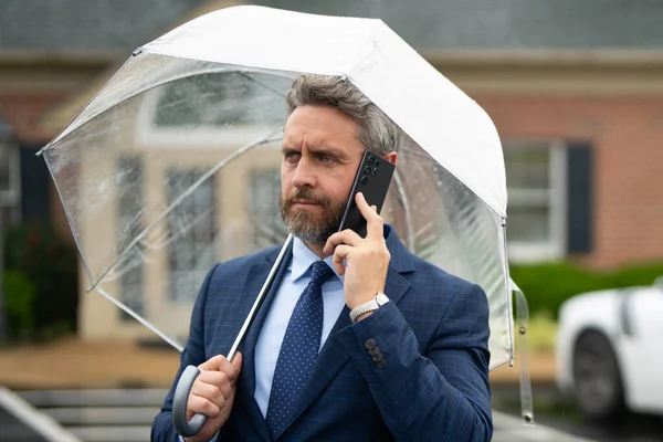 Yağmurda iş adamı. Şemsiye altında iş görüşmesi. İş adamı yağmurda dikilirken telefonda konuşur. Takım elbiseli bir iş adamı cep telefonuyla konuşuyor. Yağmurlu sokakta telefonu olan bir iş adamı.