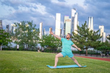 Adam dışarıda yoga yapıyor. Sporcu vücudu gerer. New York 'ta spor rutini. Sakin denge eğitimi. Şehir silueti arka planı. Yaz yoga pozu. Sakin atletik duruş. Sağlık eğitimi anı