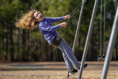 Bahar parkında sallanan neşeli çocuk. Sarı saçlı küçük bir çocuk salıncakta sallanıyor. Parkta gülümseyen mutlu çocuk. Mutlu çocukluk anları. Çocuk dışarıda oynuyor. Çocuk salıncakta eğleniyor. Çocuklar için açık hava oyunu