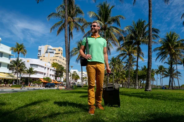 Miami sahilinde bavulla yürüyen bir turist. Yaz tatilinde valizli bir turist. Tropikal şehirde bir turist. Tropik tatil beldesinde bavullu bir turist. Turizm ve seyahat kavramı