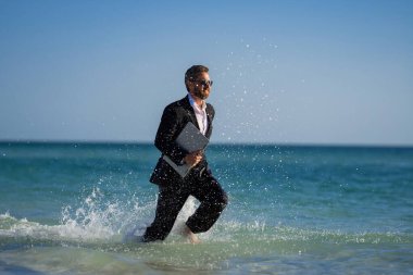 Yaz seyahati. İş başarısı. Serbest çalışma, uzaklık, online çalışma, e-çalışma. Takım elbiseli bir işadamı deniz suyunda dizüstü bilgisayarla çalışıyor. Komik bir yaz işi. Serbest seyahat.