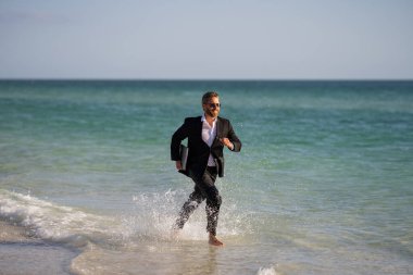 Yaz seyahati. İş başarısı. Serbest çalışma, uzaklık, online çalışma, e-çalışma. Takım elbiseli bir işadamı deniz suyunda dizüstü bilgisayarla çalışıyor. Komik bir yaz işi. Serbest seyahat.