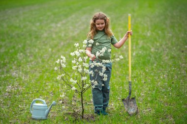 Bahçeye çocuk dikme ve sulama ağacı. Ağaç dikmenin bahar etkinliği. Kürek ve su bidonlarıyla çocuk işi. Çocuk meyve ağacı dikiyor. Bahçıvan çocuklar. Çocuk yetiştirme ve ağaç bakımı
