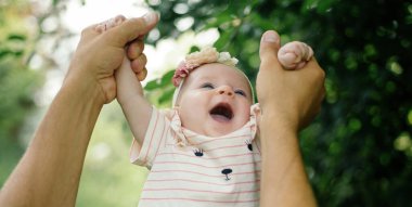 Mutlu bebek ebeveynlerin elinde. Küçük kızımızın ailesi dışarıda kaynaşıyor. Ebeveyn ve bebek. Bebek mutluluğu ve bakım