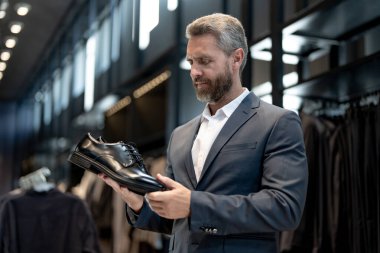 Moda mağazasında olgun bir adam farklı ayakkabı stillerini değerlendirir. İş adamı kendine güvenerek şık ayakkabıları bir ayakkabı mağazasında seçer. Resmi görünmek için klasik deri ayakkabılar. Resmi ayakkabılar. Deri ayakkabılar.