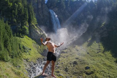 Kaslı adam temiz hava soluyor. Ellerini kaldırıp hava soluyan yakışıklı bir üstsüz model. Seksi adam doğa üzerine meditasyon yapıyor. Şelalenin yanında sakin bir nefes al. Doğada sağlık ve nefes alma.