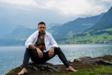 Dağ gölü manzarasında dinlenen adam. Seksi, üstsüz, kaslı, İspanyol, özgürlük kavramı. İnsan doğal ortamda tefekkür eder. Erkek dayanıklılığı ve dışarıda yalnızlık