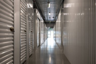 Modern bir depolama tesisinin içinde uzun bir koridor. Kapıları metal kapaklı boş depo koridoru. Kiralık temiz ve güvenli depolama birimleri. Sanayi ile simetrik depolama koridoru