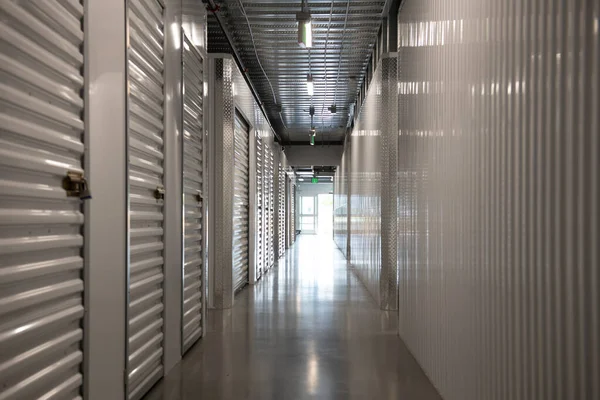 Modern bir depolama tesisinin içinde uzun bir koridor. Kapıları metal kapaklı boş depo koridoru. Kiralık temiz ve güvenli depolama birimleri. Sanayi ile simetrik depolama koridoru