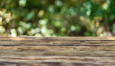 Green background with wooden table. Wooden table in the foreground with a lush, green park scene in the background. Beautiful natural summer background with empty wooden table in nature outdoor
