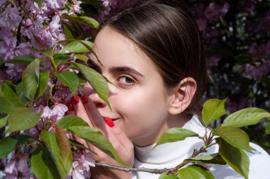 Çiçeklerin arasında gülümseyen bahar kadını. Bahar kadını romantik portresi bahçede. Çiçekli sakura dalıyla bahar kadını güzelliği. Bahar kadını doğada mutluluk