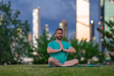 Adam huzurlu bir ifadeyle meditasyon yapıyor. Doğada yoga yapan bir adam. Lotus meditasyon pozunda oturan adam. Adam sakin ve sağlıklı anın tadını çıkarıyor.