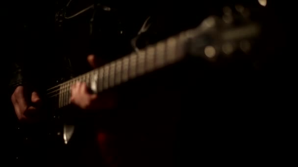 Músico masculino tocando uma melodia na guitarra close-up em um fundo preto arrancar as cordas em uma jaqueta de couro — Vídeo de Stock