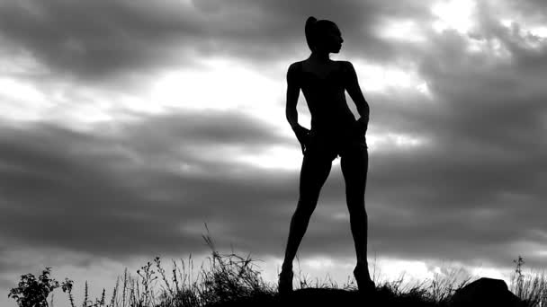 štíhlá holka foto model představuje pro focení na pozadí zatažené oblohy na pole, černé a bílé video, silueta ženy