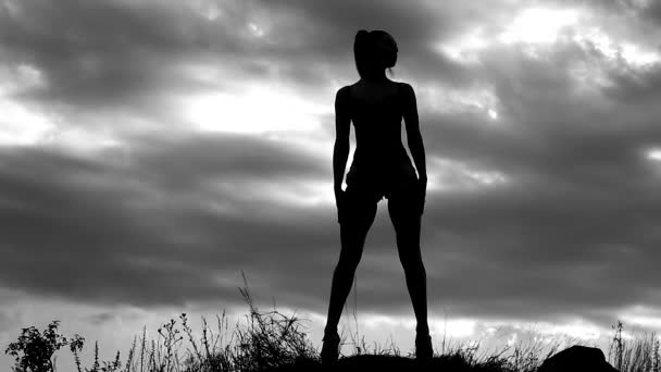 Karcsú lány fénykép modell jelentő egy fotózásra, a háttérben egy felhős ég a mező, a fekete-fehér video, a sziluettje egy nő — Stock videók
