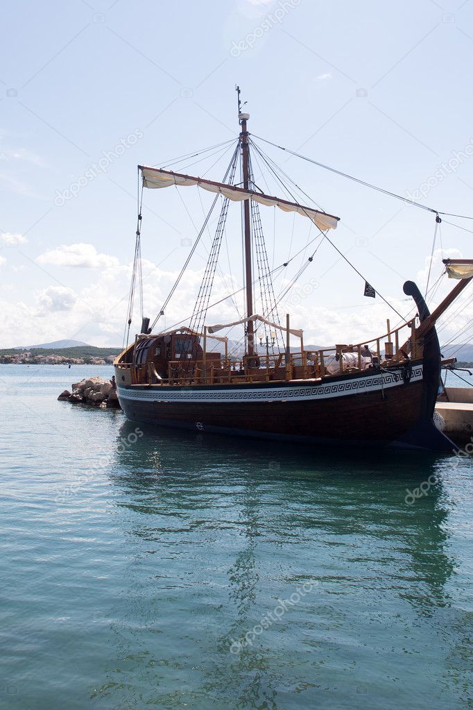 Photo Closeup Of One Beautiful Wooden Antiquated Sailing Ship With Shorten Sails Lies Idle In Dry Dock At Seashore Silhouetted Against Blue Sea At Day Time Over Seascape Background Vertical Picture Photo Closeup Of One Beautiful Wooden Antiquated Sailing Ship With Shorten Sails Lies Idle In Dry Dock At Seashore Silhouetted Against Blue Sea At Day Time Over Seascape Background Vertical Picture