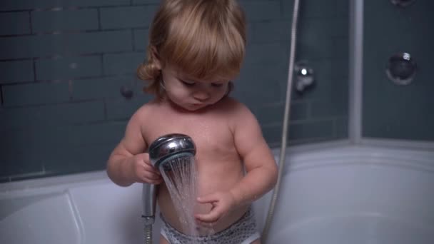 4K little curly cute boy takes a shower in the bath, pour water over his arm, smiling and waving at the camera — Stockvideo