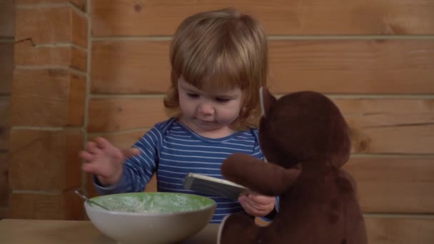 4К милый маленький ребенок смотрит в мобильный телефон и кормит медведя творогом со сметаной — стоковое видео