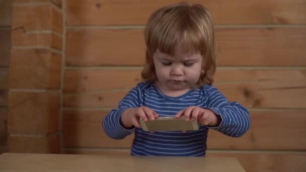 4k kleine krullend baby kijken naar de telefoon in een houten huis — Stockvideo