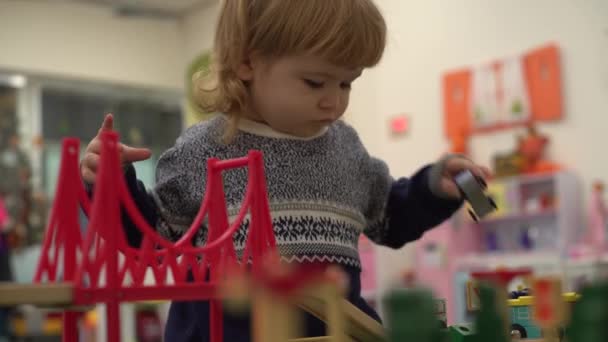 4K hermoso niño en el jardín de infantes lleva el coche de la carretera de juguete y el puente — Vídeo de stock