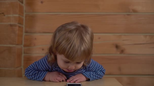 4K красивий маленький хлопчик дивиться на мобільний телефон, телефон піднімається і виходить з рамки — стокове відео