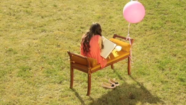 Malá dívka umělec kreslí obrázek v poznámkovém bloku na gauči v trávě — Stock video